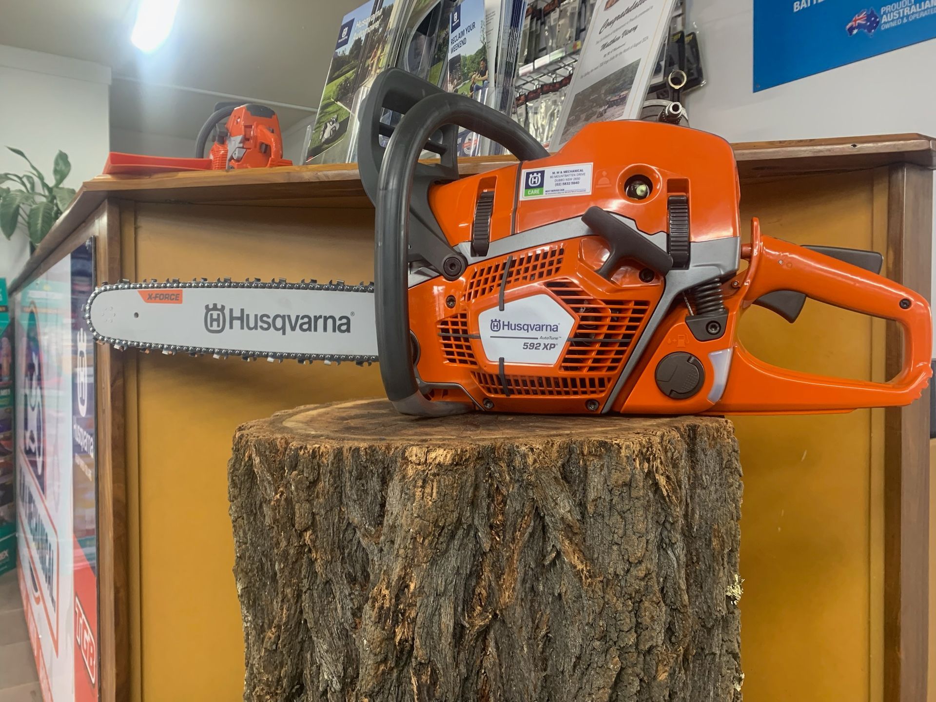 Orange Husqvarna chainsaw on a tree stump in a store— M.M & Mechanical in Dubbo, NSW