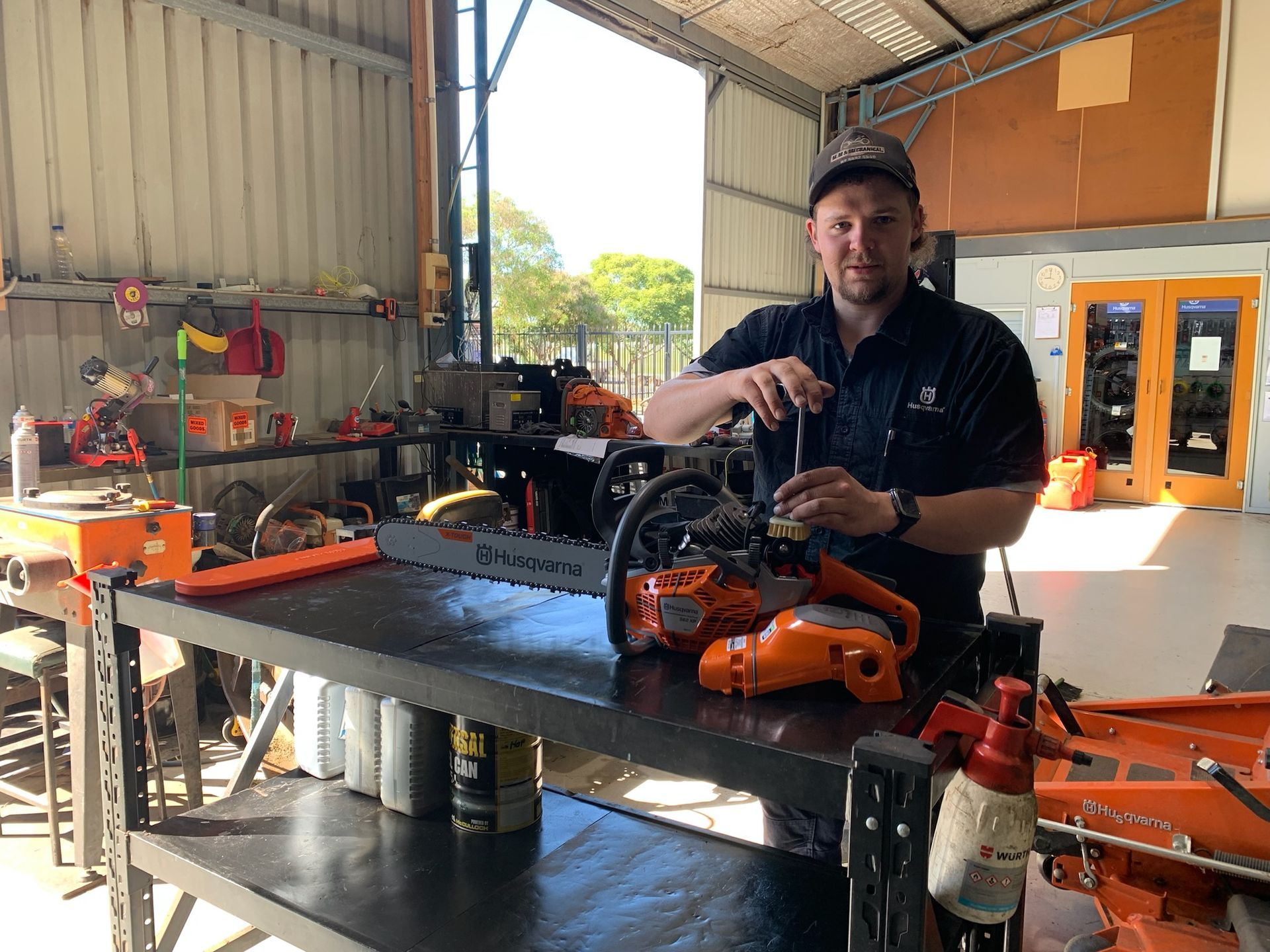 Man working on a chainsaw in a workshop; various tools, saws, and parts visible— M.M & Mechanical in Dubbo, NSW