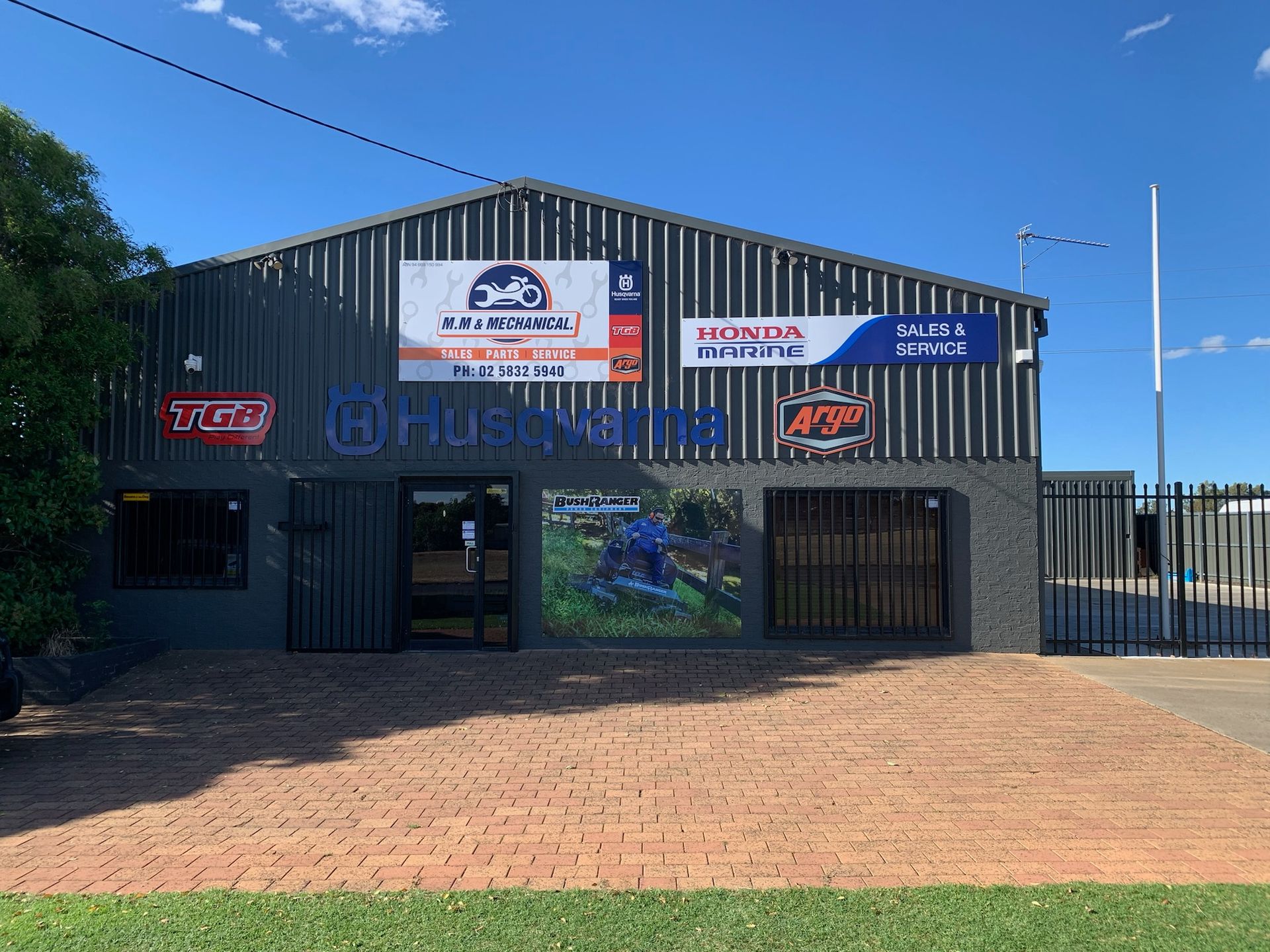 A grey building with signs for motorcycles and services; a Husqvarna logo and a partially visible motorcycle poster— M.M & Mechanical in Dubbo, NSW
