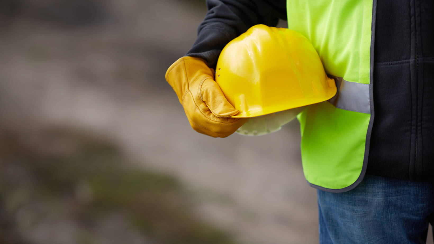 A construction worker is holding a yellow hard hat and gloves.