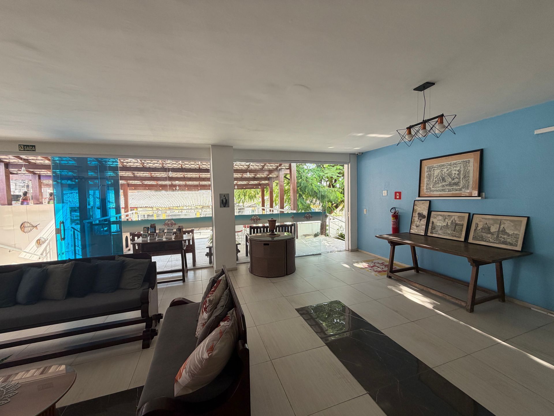 Sala de estar iluminada com parede de destaque em azul, sofá, escrivaninha e vista aberta para um pátio.