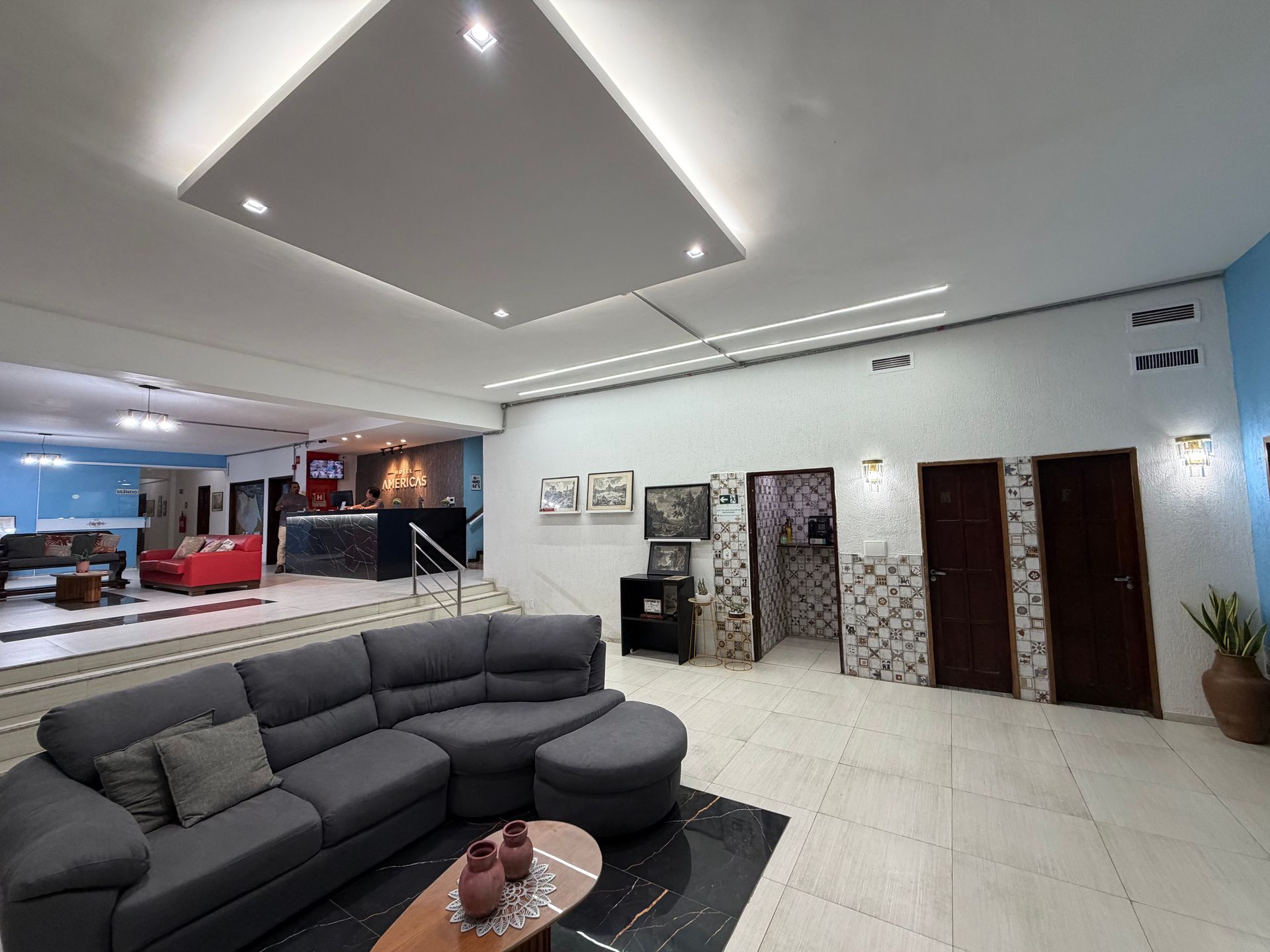 Hall de entrada moderno com sofá modular cinza, mesa de centro, piso de azulejo e portas de elevador com iluminação embutida.