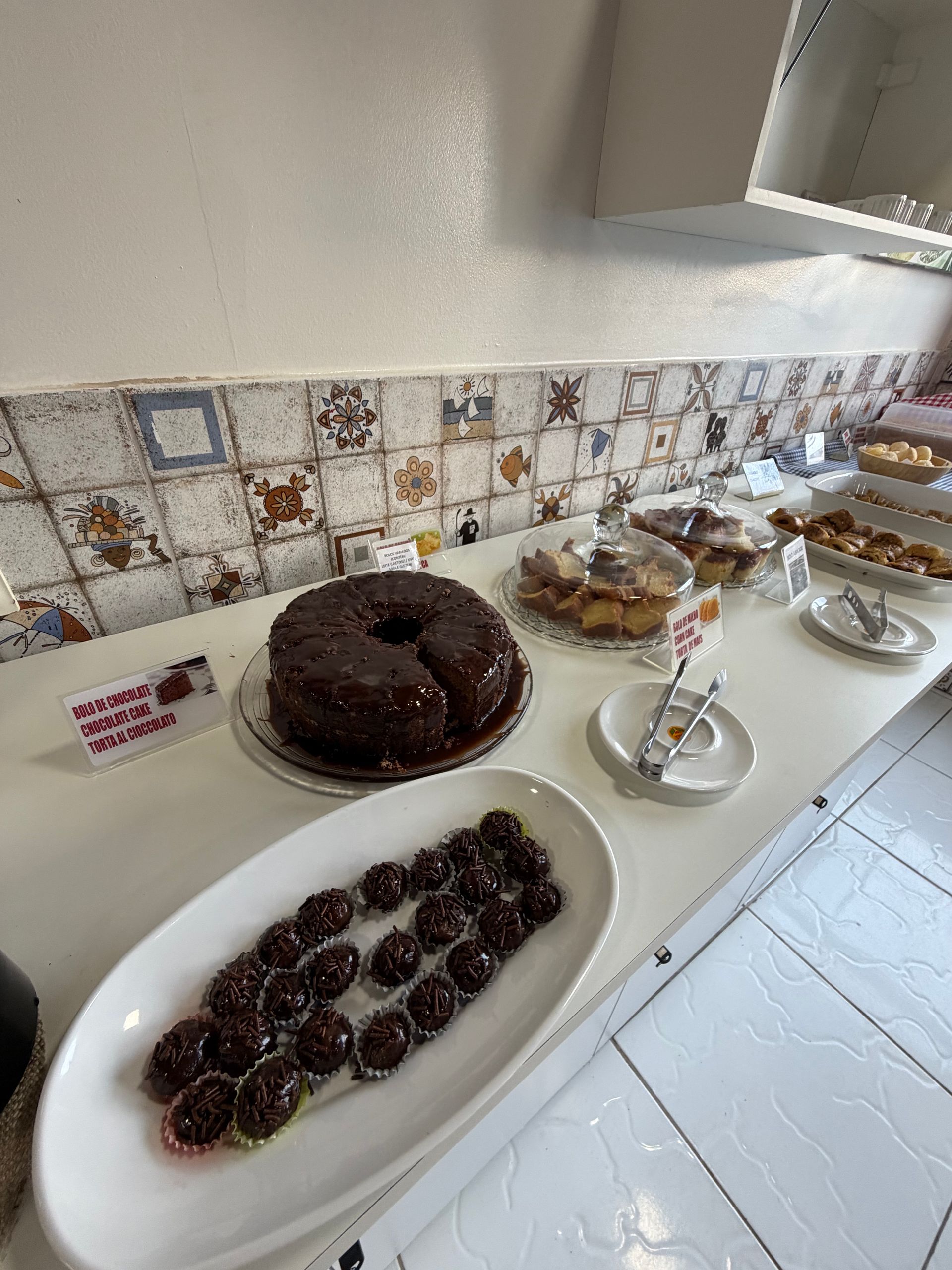 Buffet de sobremesas com bolo de chocolate, torta de frutas vermelhas, doces e parfait em um balcão branco.