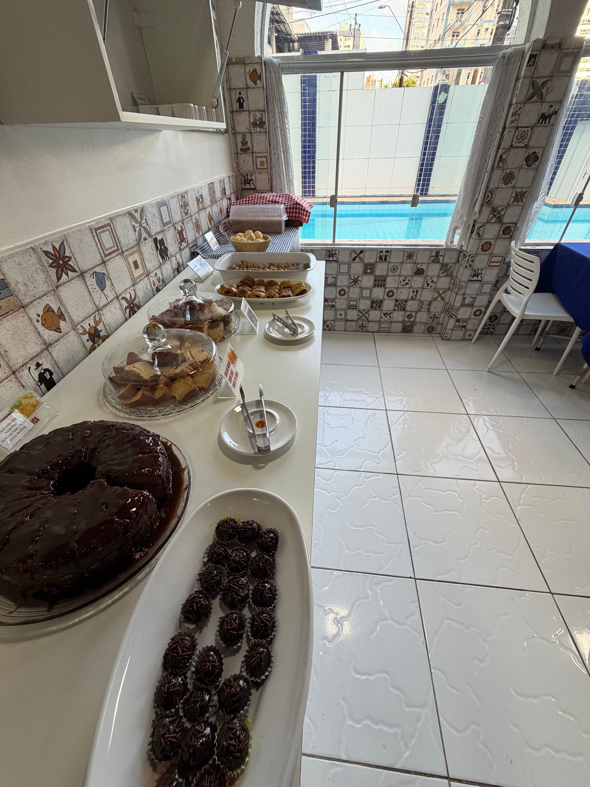 Um bufê disposto em um balcão de azulejos ao lado de uma janela, com doces, sobremesas e serviço de chá.