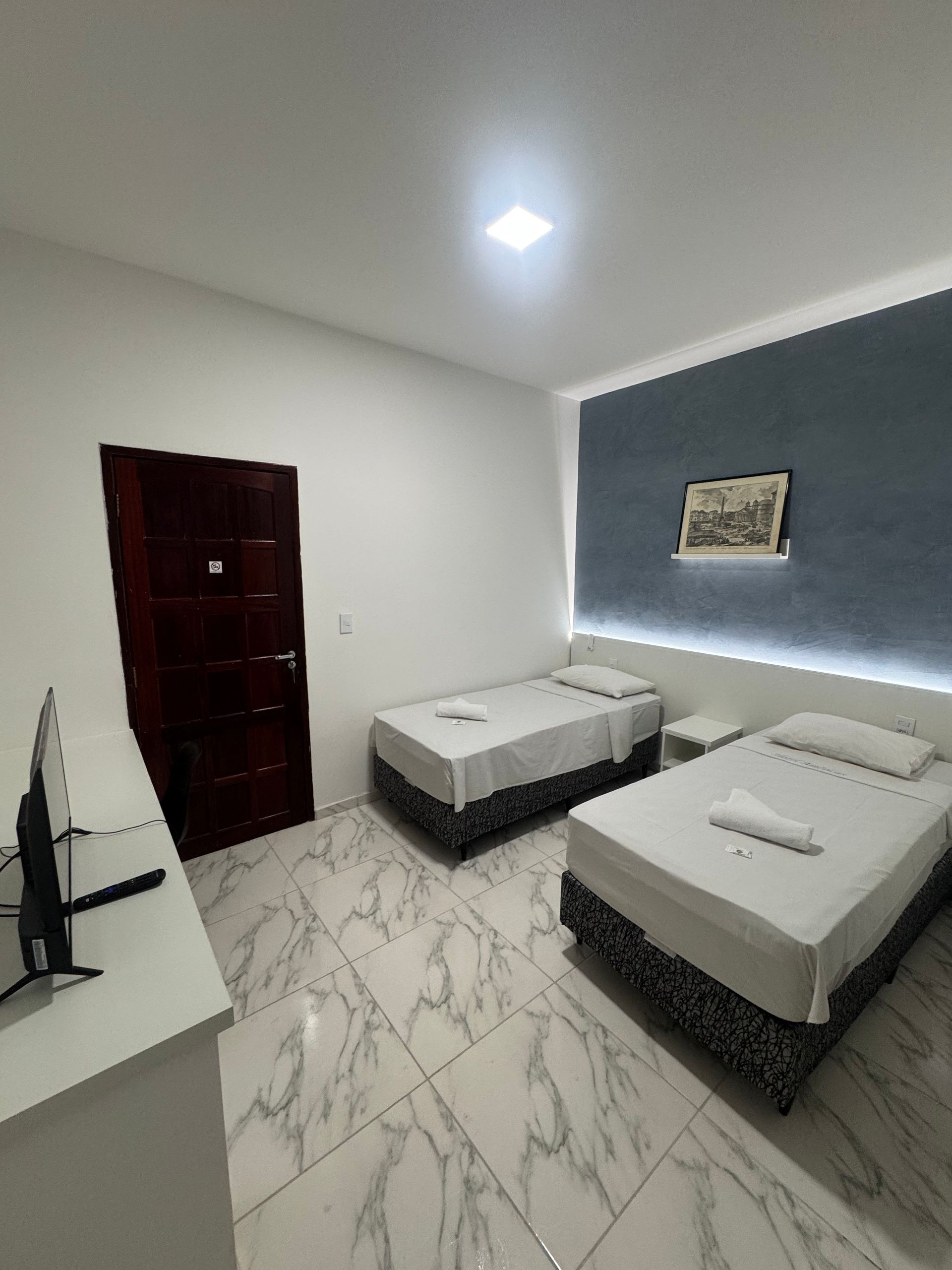 Quarto com duas camas de solteiro, piso de mármore branco, paredes cinza e porta de madeira escura.