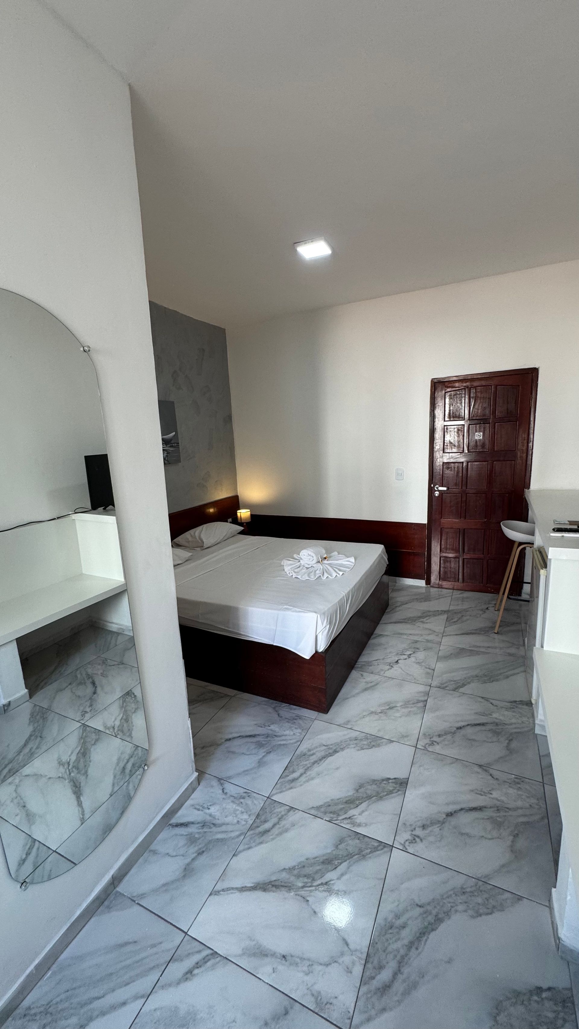 Quarto moderno com cama, piso de mármore, paredes brancas, cômoda e porta vermelha na parede do fundo.