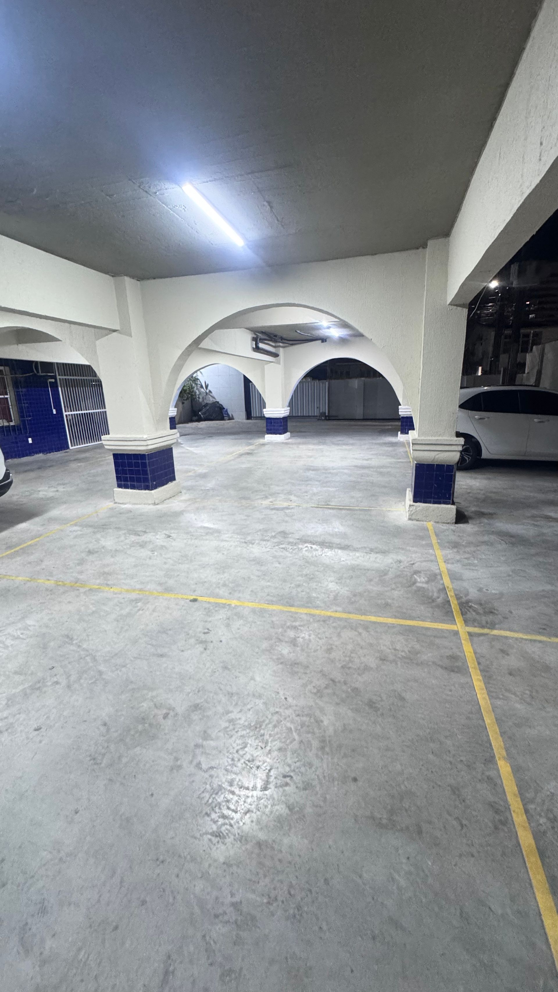 Estacionamento coberto vazio com arcos brancos, piso de concreto e faixas demarcadas em amarelo à noite.