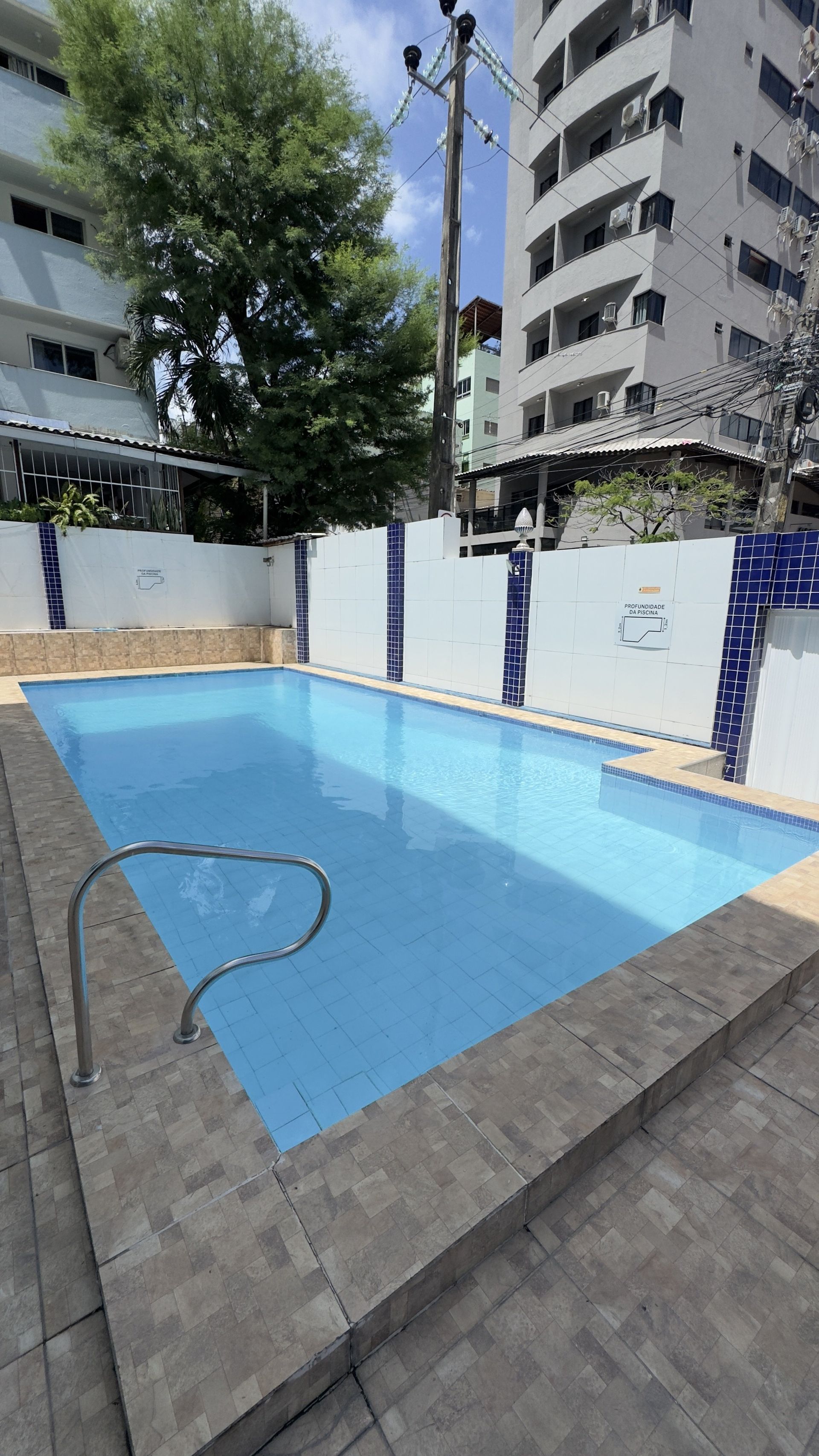 Pequena piscina externa com água azul, deck de azulejos e prédios de apartamentos ao redor.
