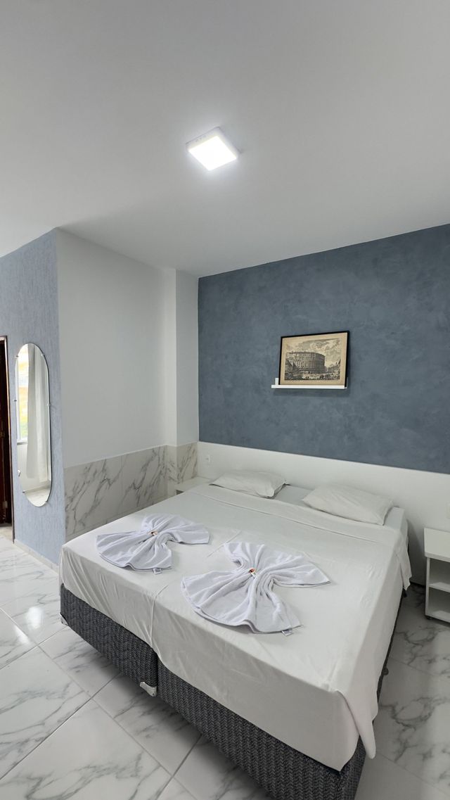Quarto moderno com roupa de cama branca, parede de destaque azul e obras de arte na parede.