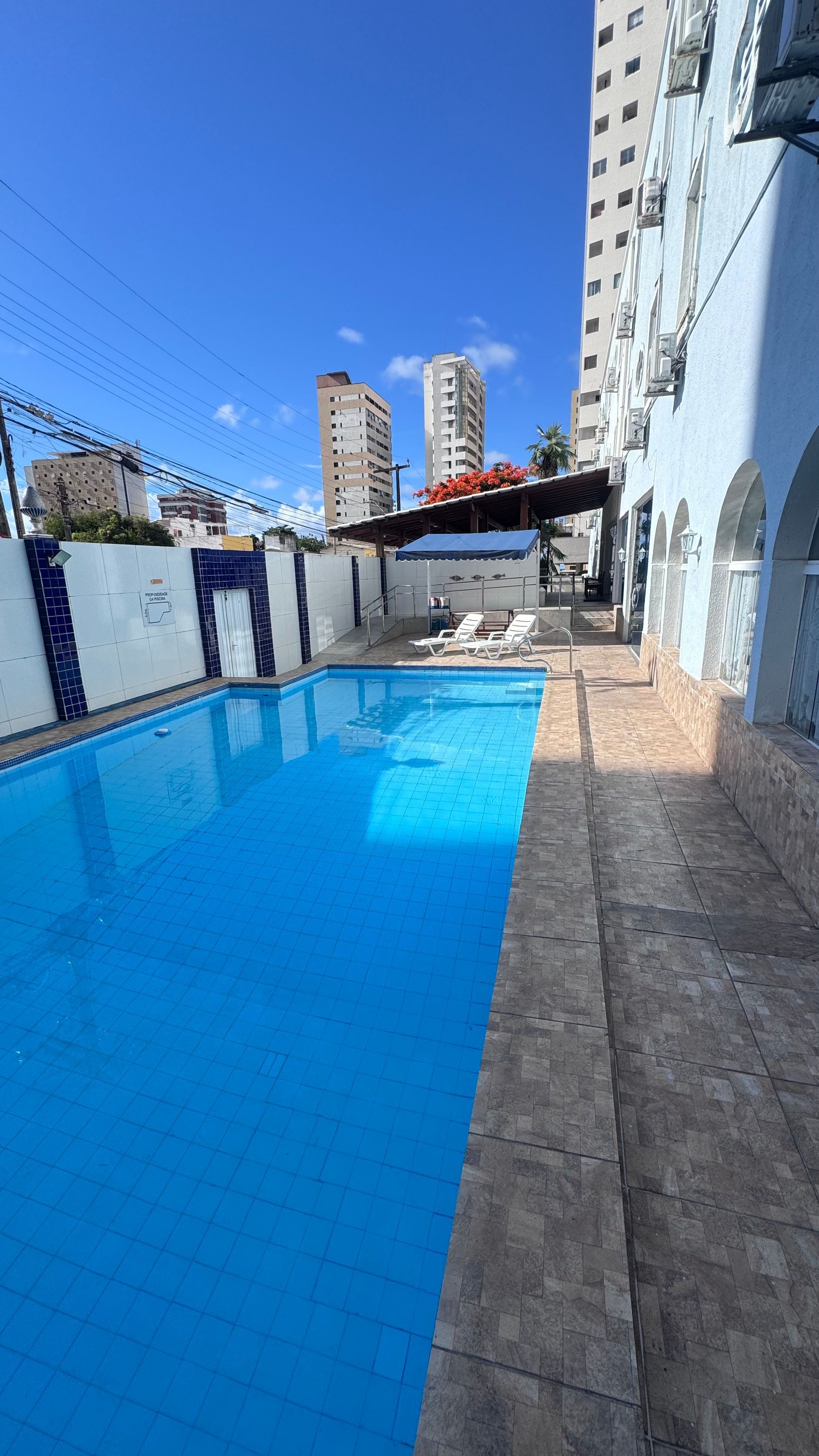 Piscina ao ar livre na cobertura com água azul ao lado de prédios residenciais sob um céu claro.