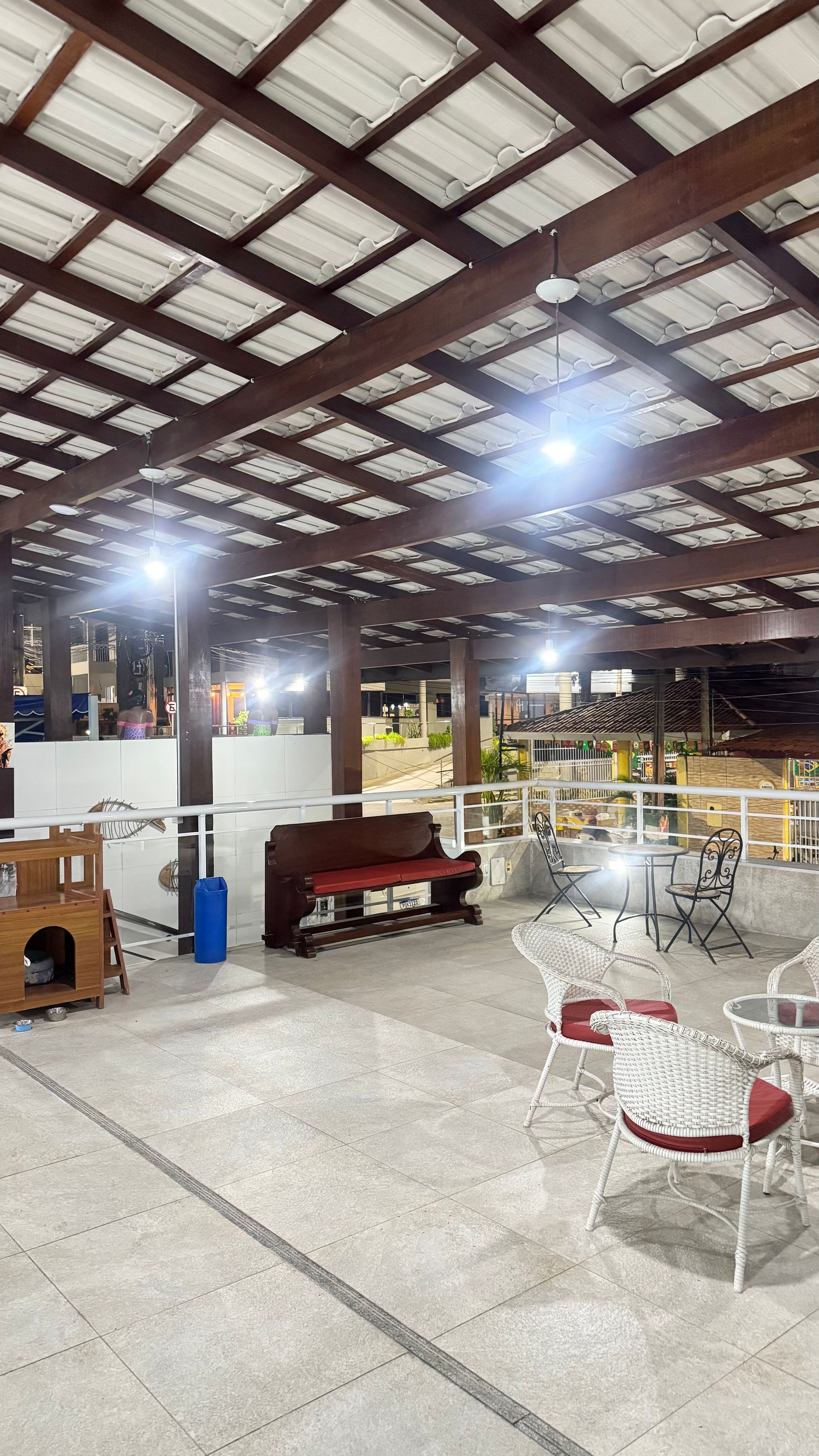 Arena esportiva coberta com iluminação intensa, vigas metálicas no teto e fileiras de cadeiras brancas e vermelhas próximas à quadra.