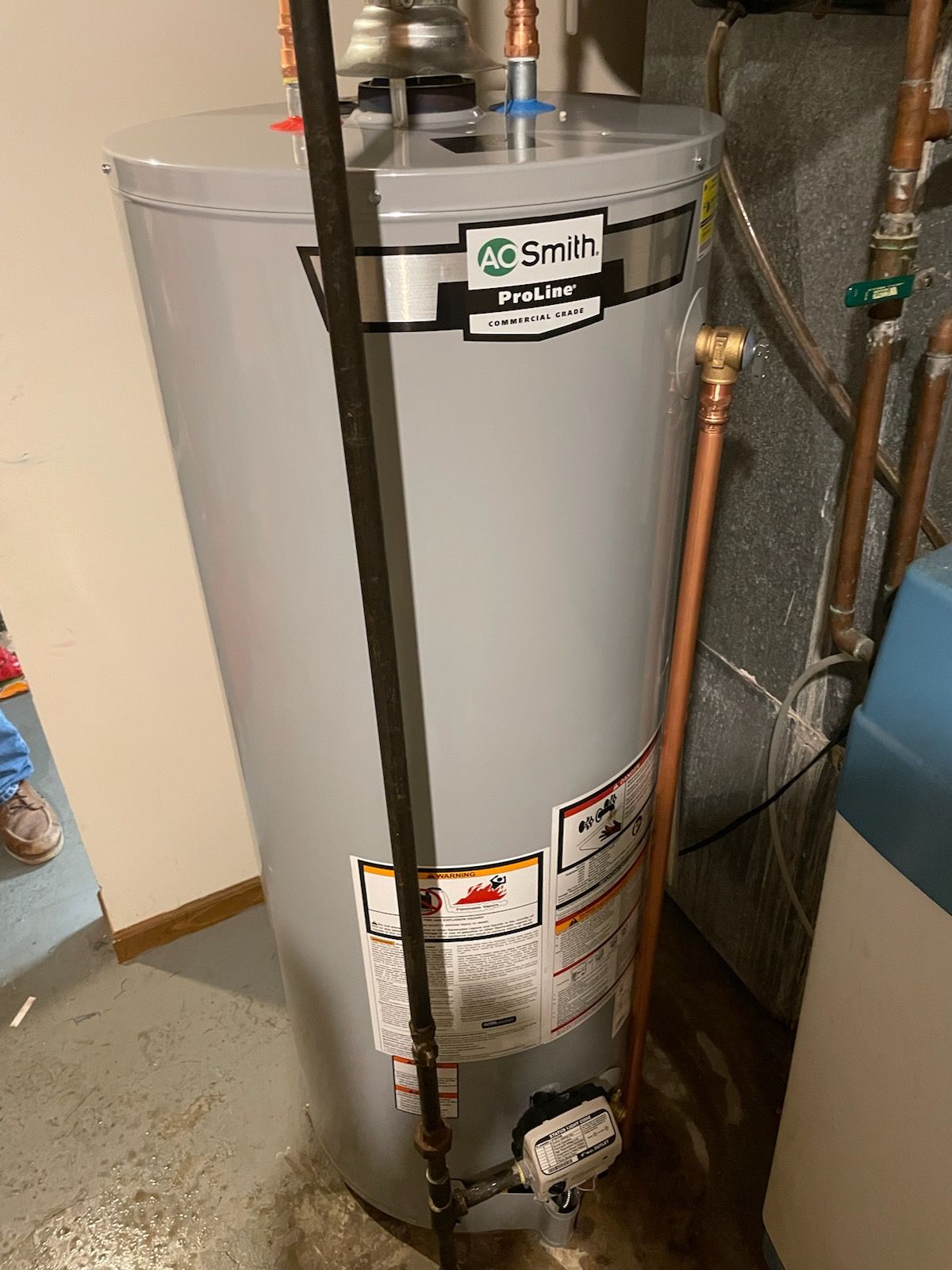 A water heater is sitting in a basement next to pipes.