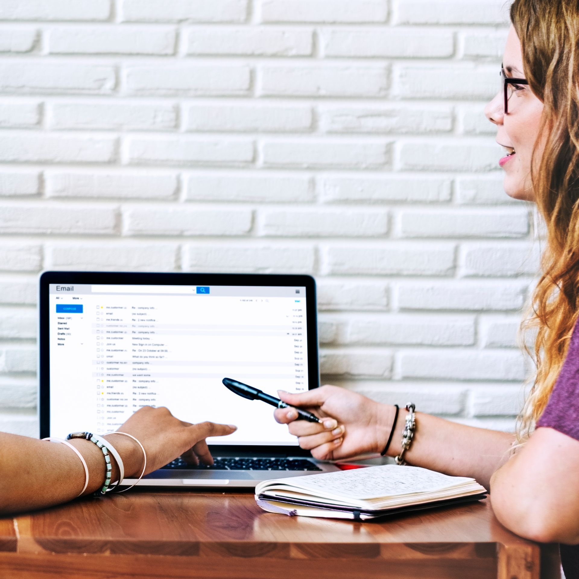 Two women are sitting at a table with a laptop and a cell phone