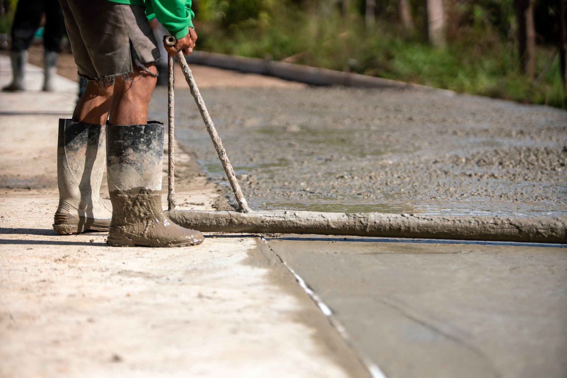A man is spreading concrete on a sidewalk with a broom.