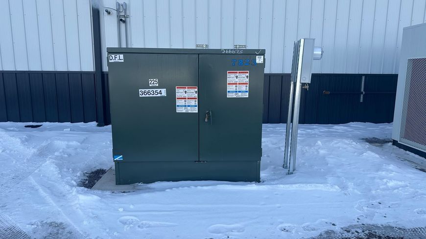 A green box is sitting in the snow in front of a building.