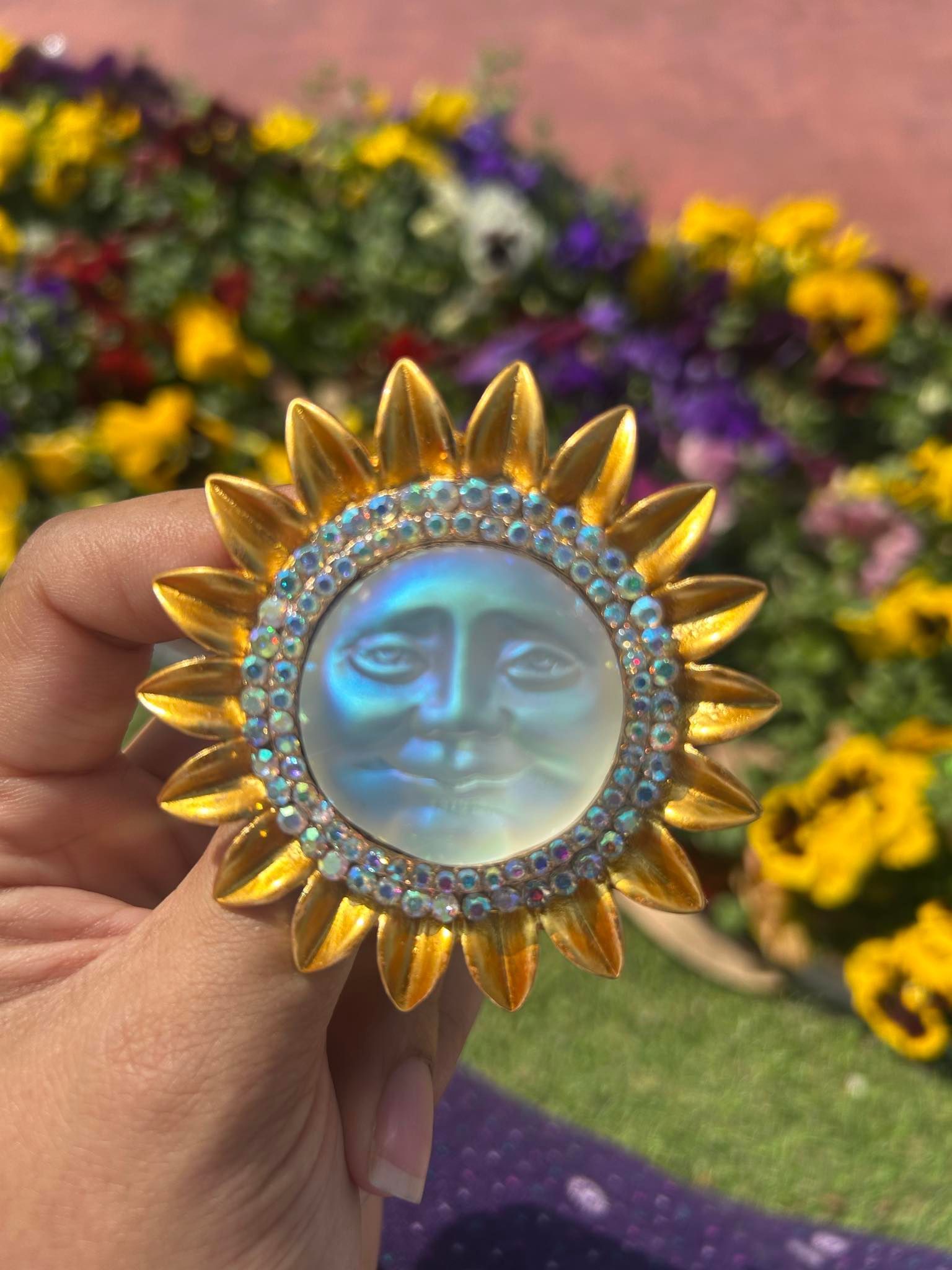 A person is holding a sun with a face on it in front of a field of flowers.