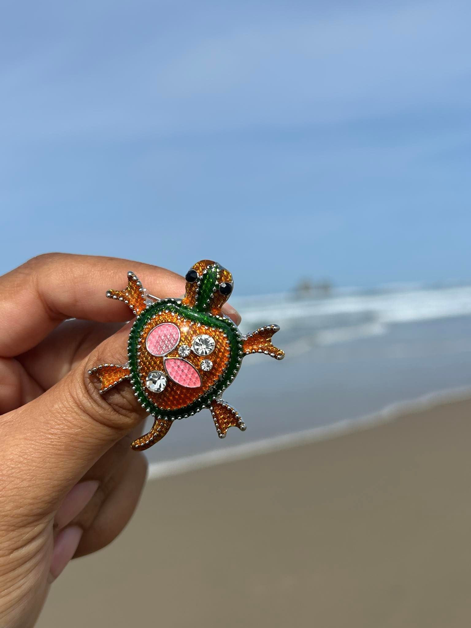 A brooch in the shape of a turtle is sitting on a mossy branch.