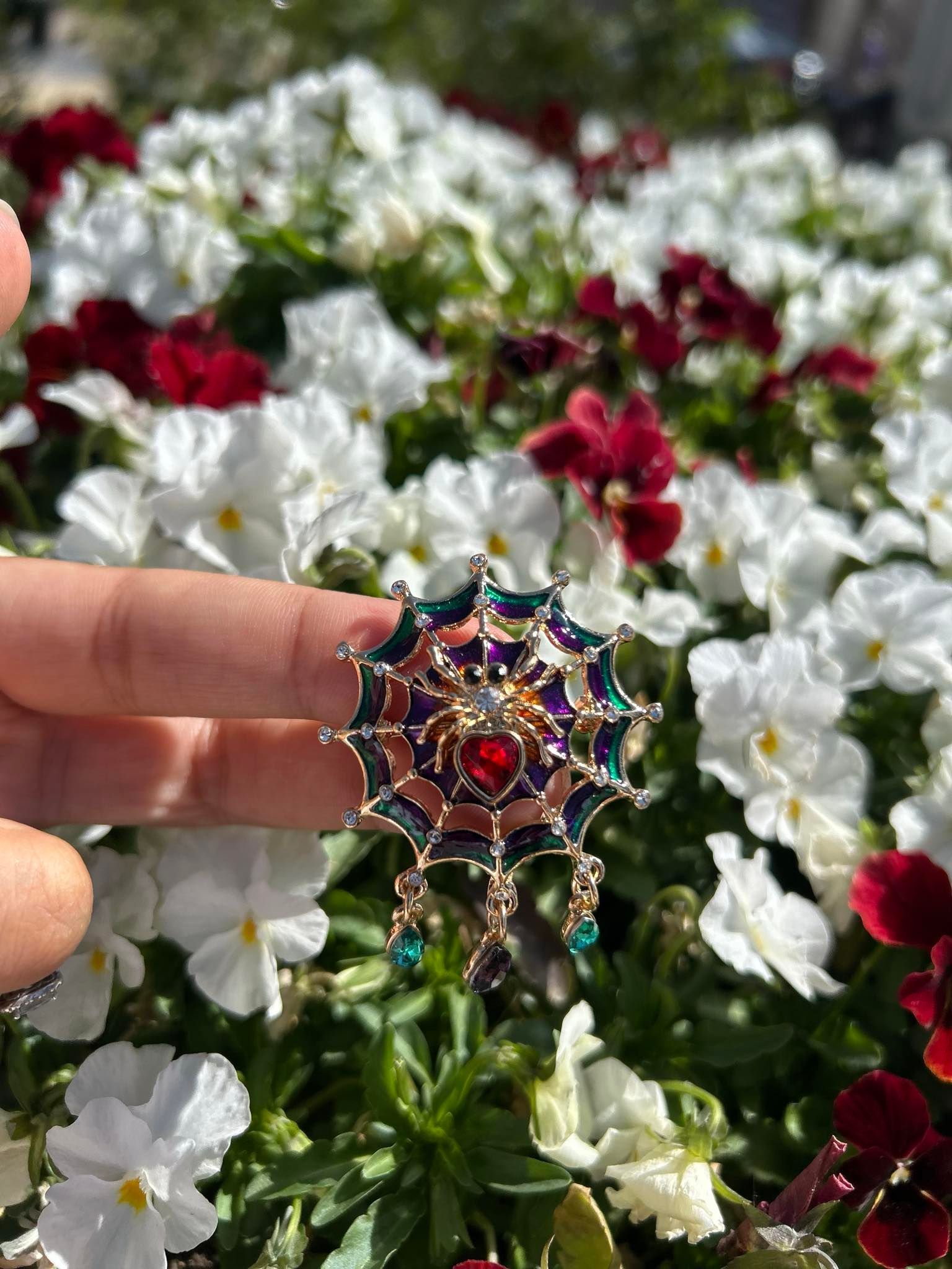 A person is holding a brooch in front of a field of flowers.