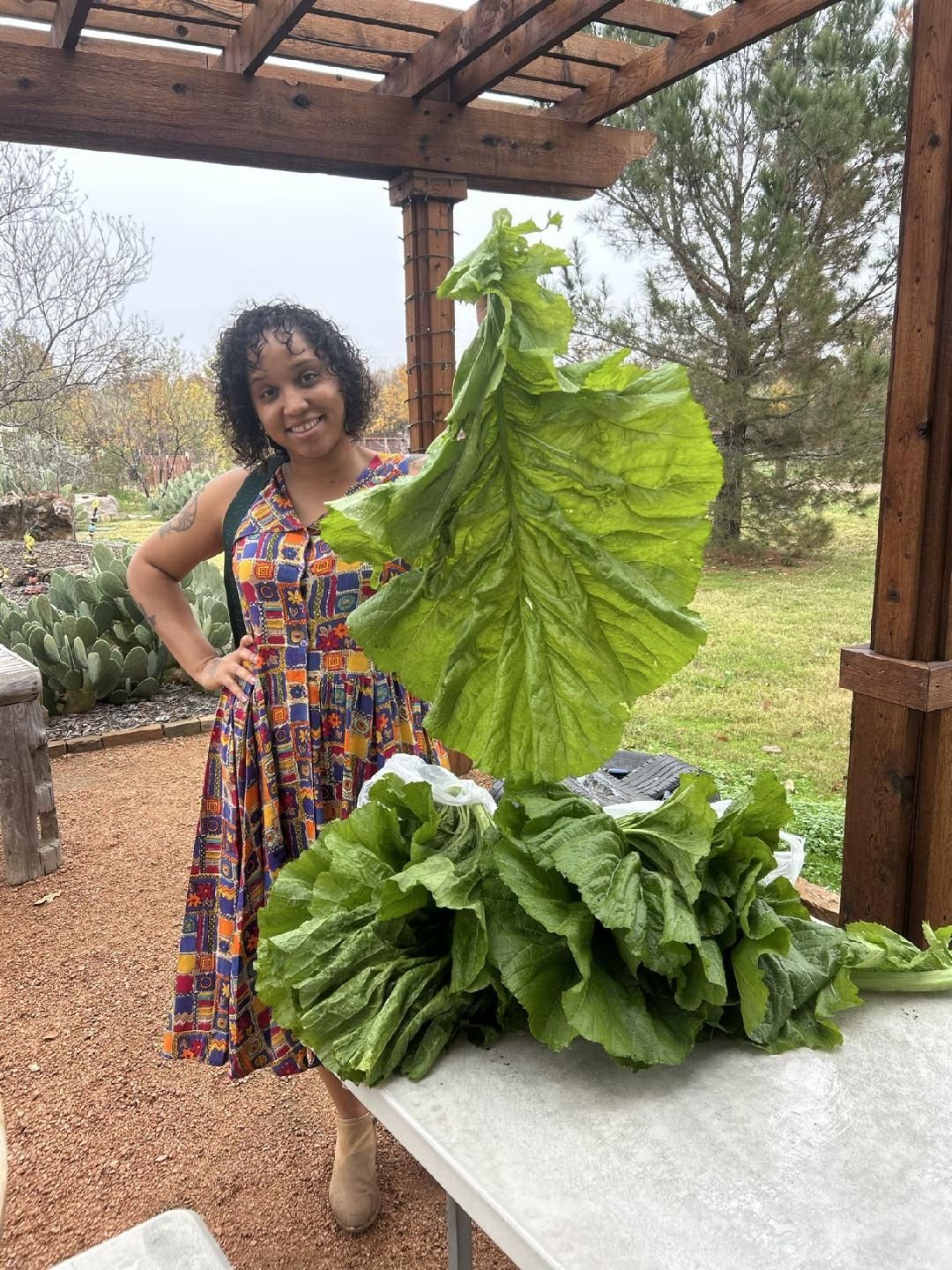 A woman in a dress is standing next to a table holding a large green leaf.