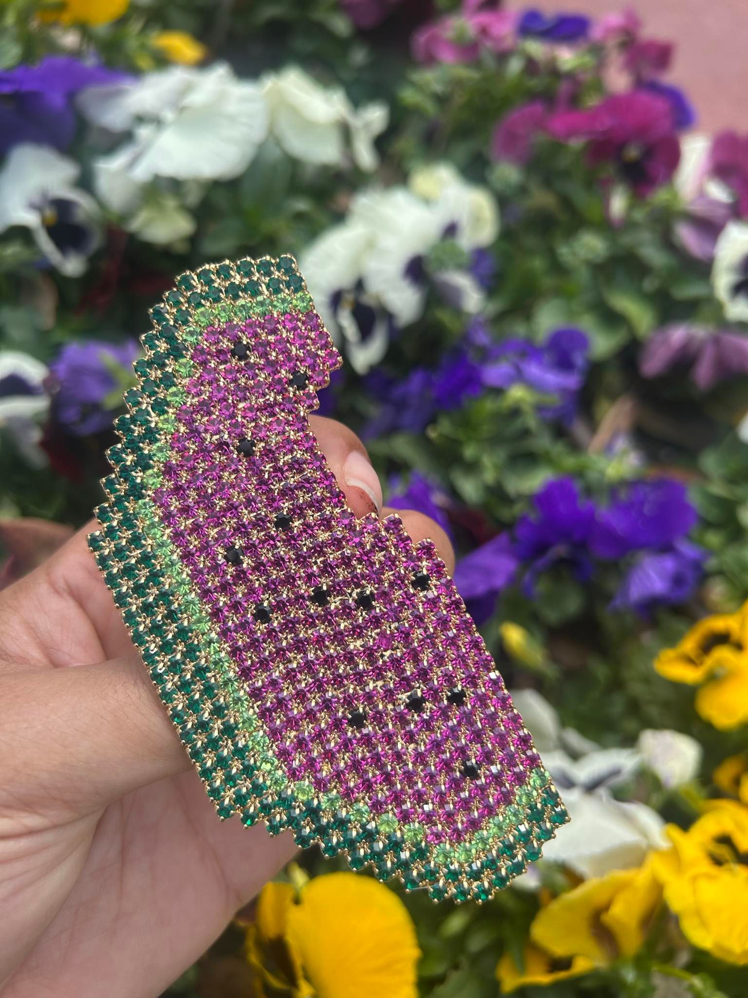 A person is holding a brooch in the shape of a watermelon in front of flowers.
