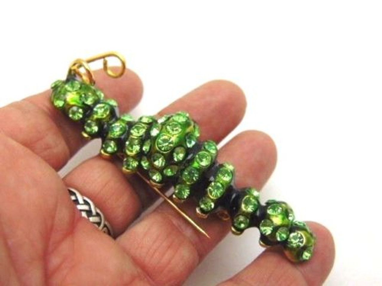 A close up of a brooch with green rhinestones on a white background