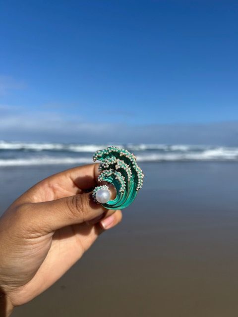 A person is holding a green wave with a pearl in their hand.