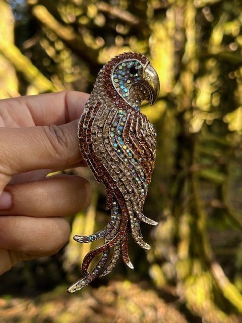 A brooch in the shape of a parrot is sitting on a mossy tree trunk.