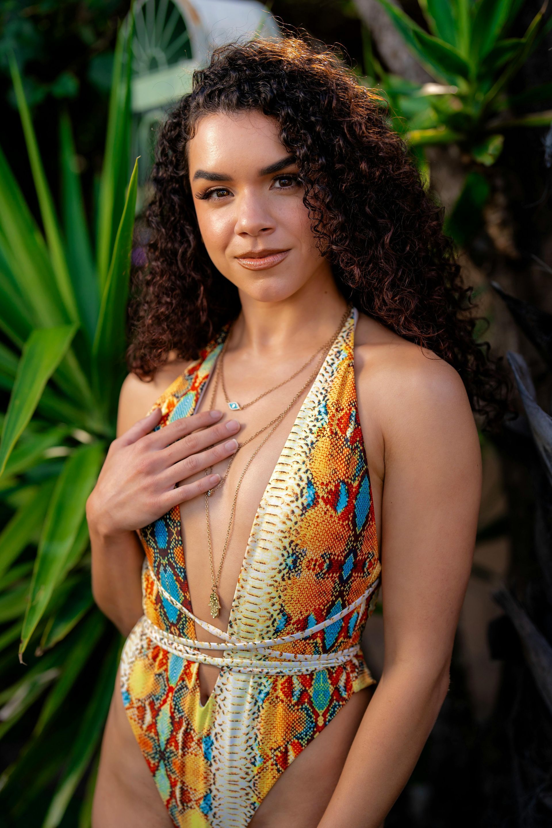 A woman in a colorful swimsuit is standing in front of a plant.