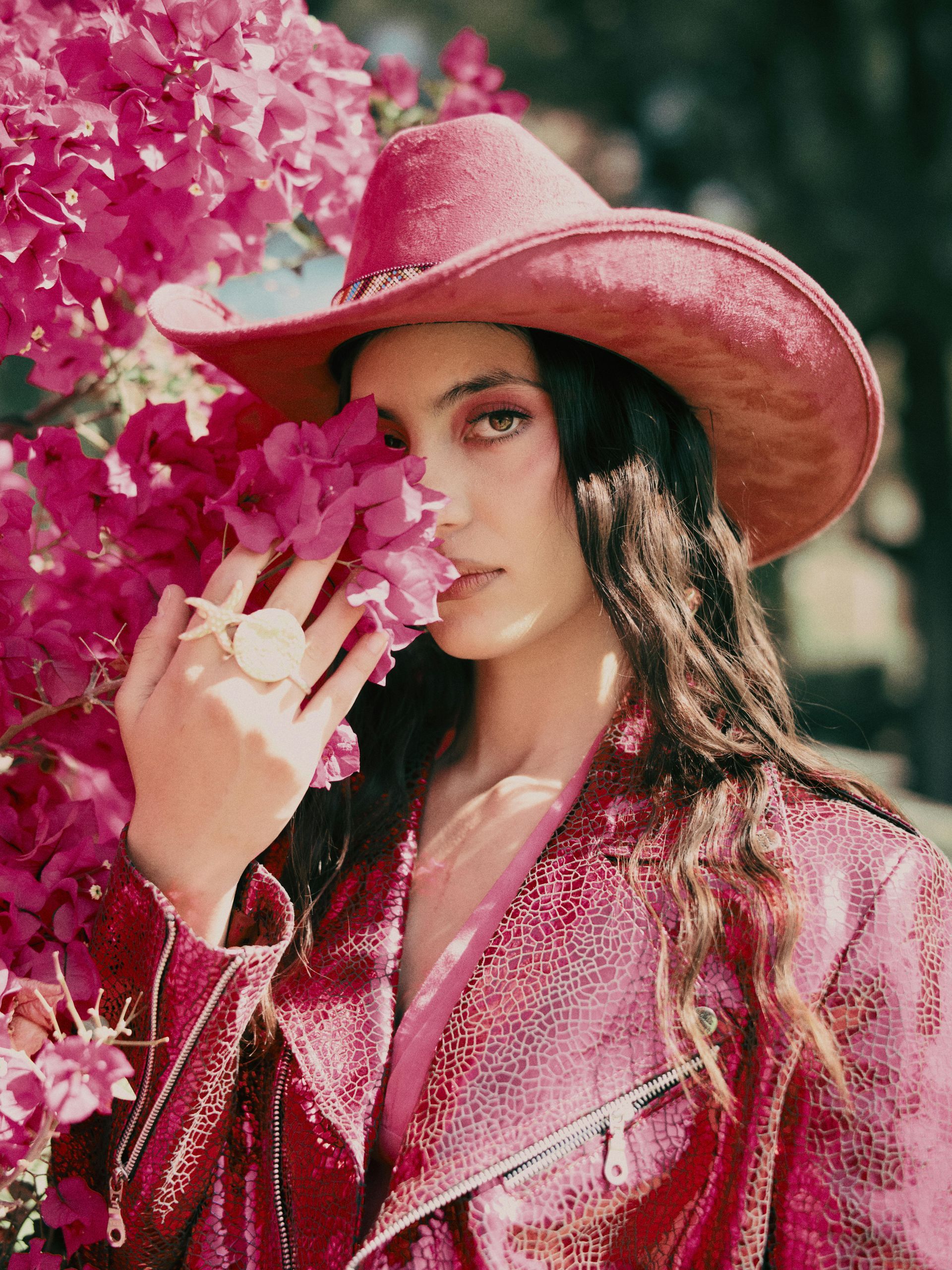 A woman wearing a pink cowboy hat and a pink jacket is covering her face with pink flowers.