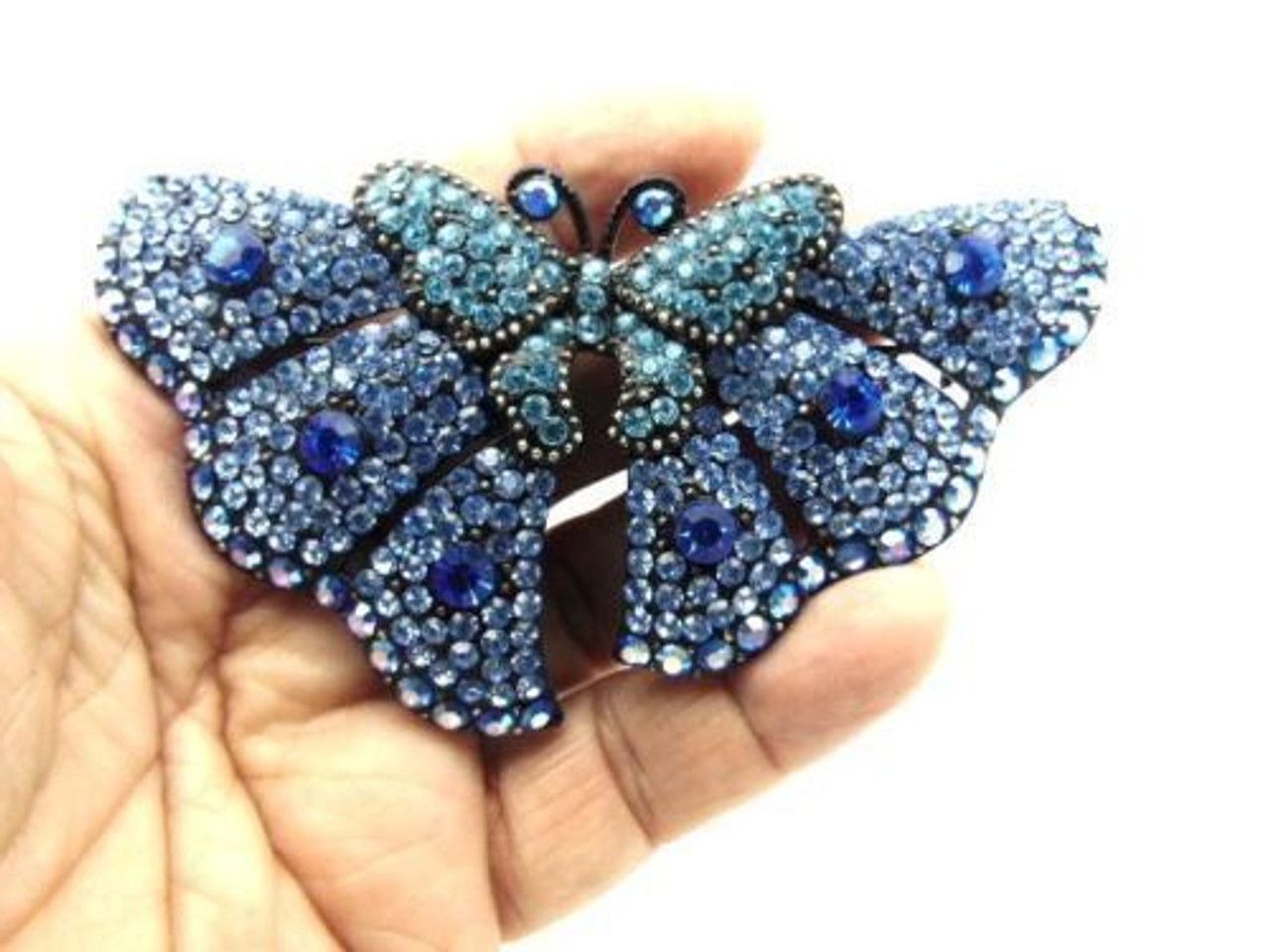 A person is holding a blue butterfly brooch in their hand