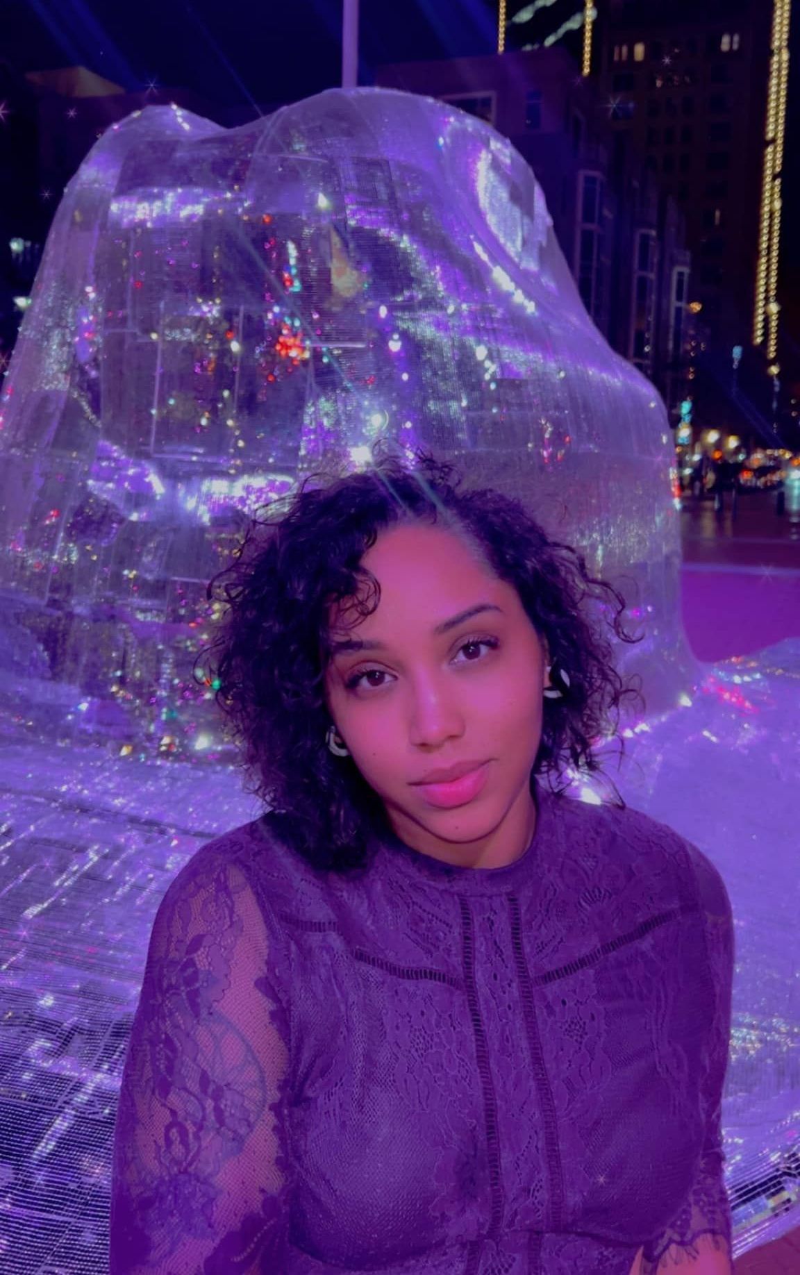 A woman in a purple dress is standing in front of a large ice sculpture.
