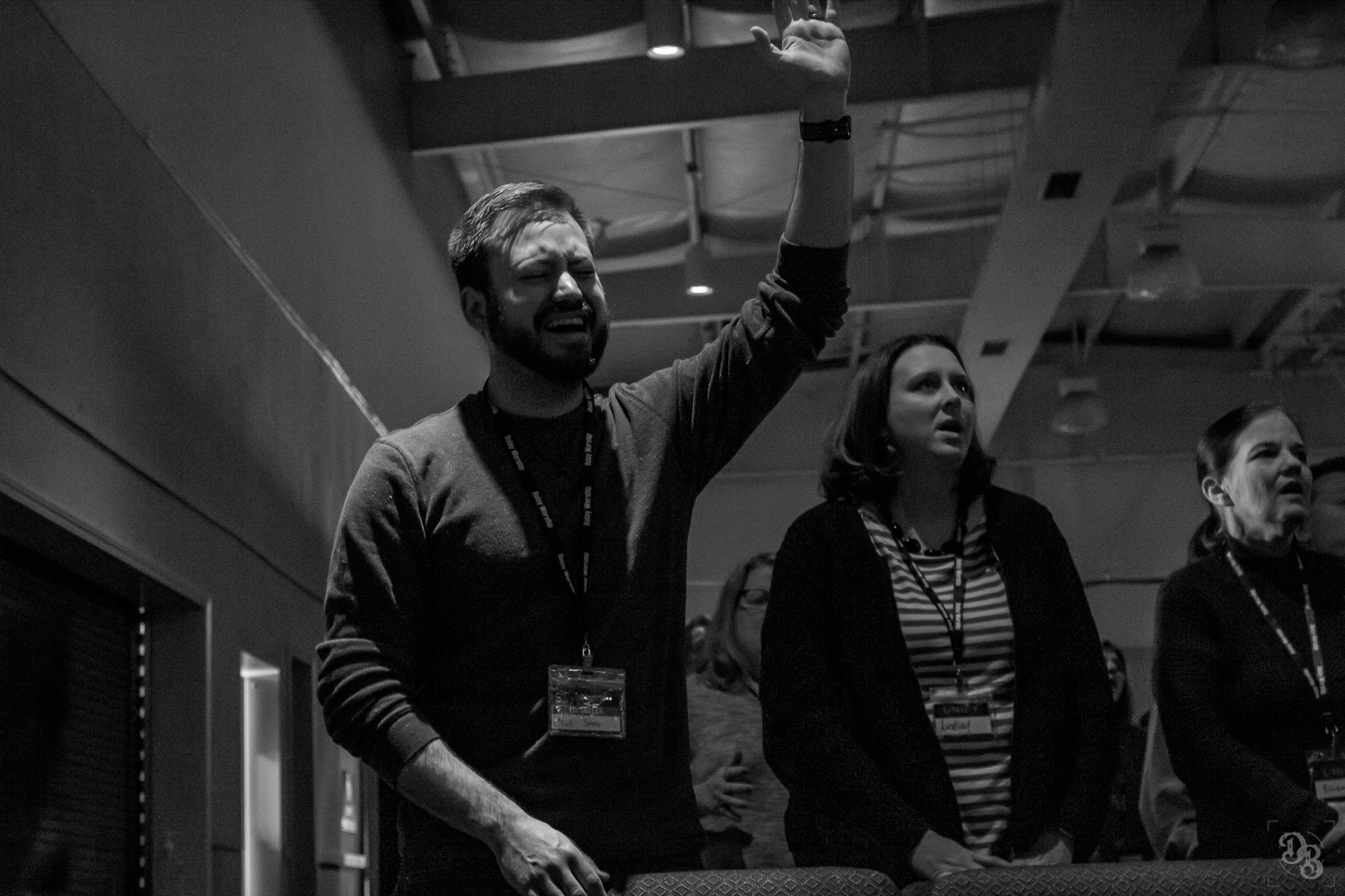 Black and white photo of people in a room standing with heads tilted back, one person with an arm raised in a gesture.
