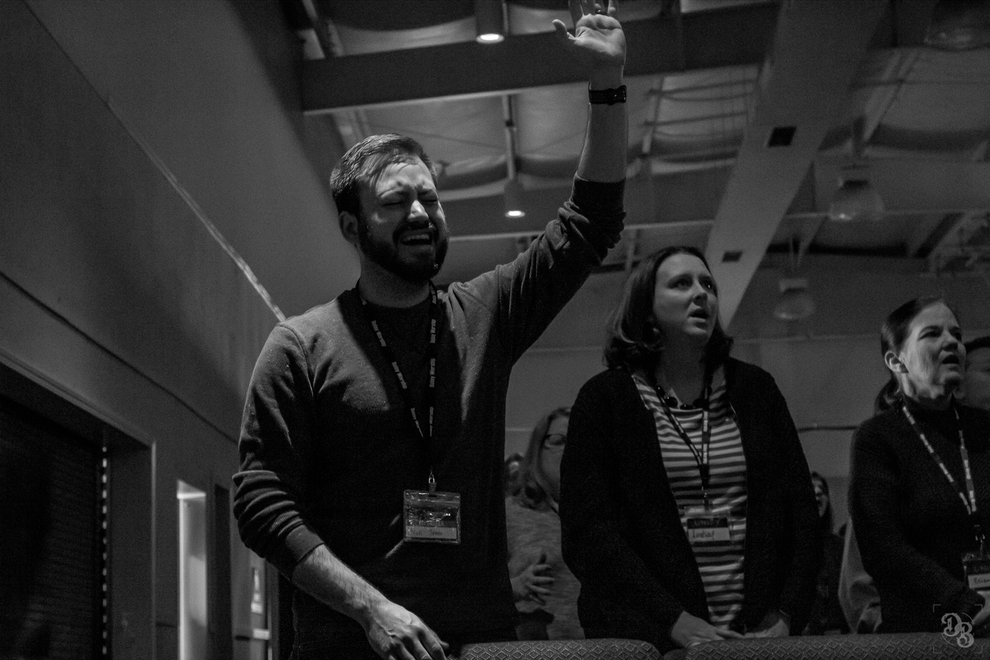 Black and white photo of people in a room standing with heads tilted back, one person with an arm raised in a gesture.