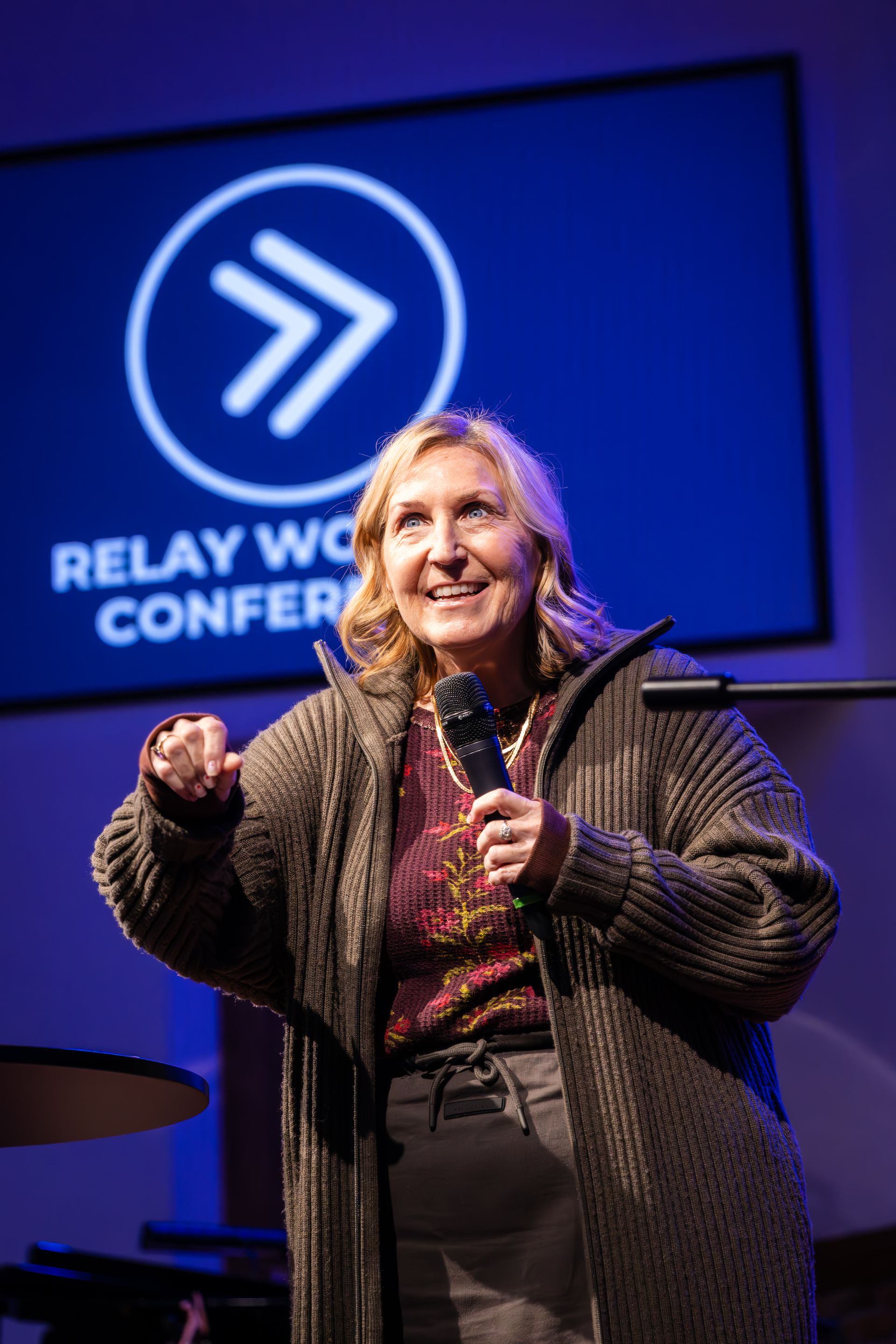 A speaker holds a microphone and gestures while presenting on stage at the Relay Women’s Conference.