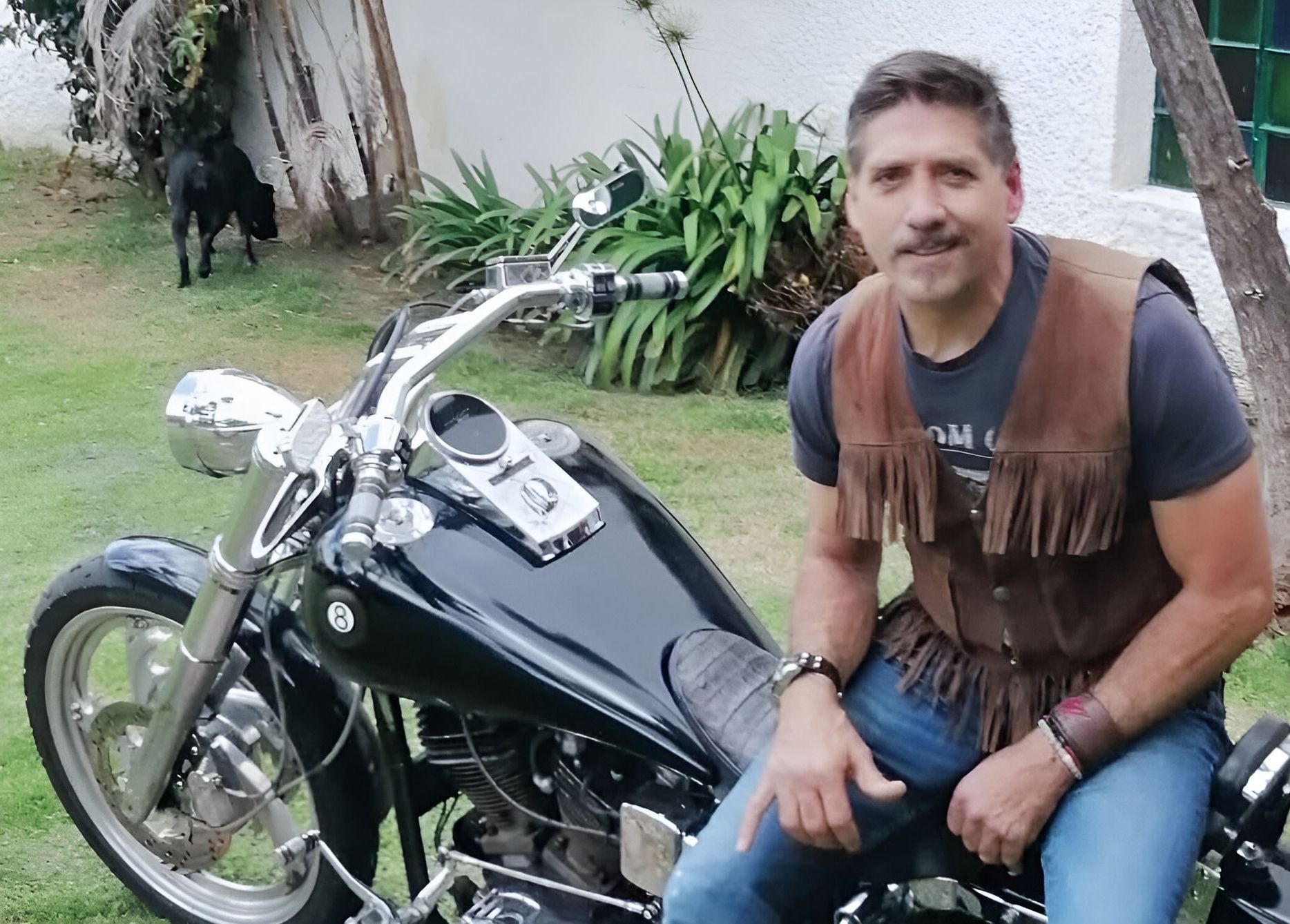 Un hombre sentado en una motocicleta negra con un perro al fondo.