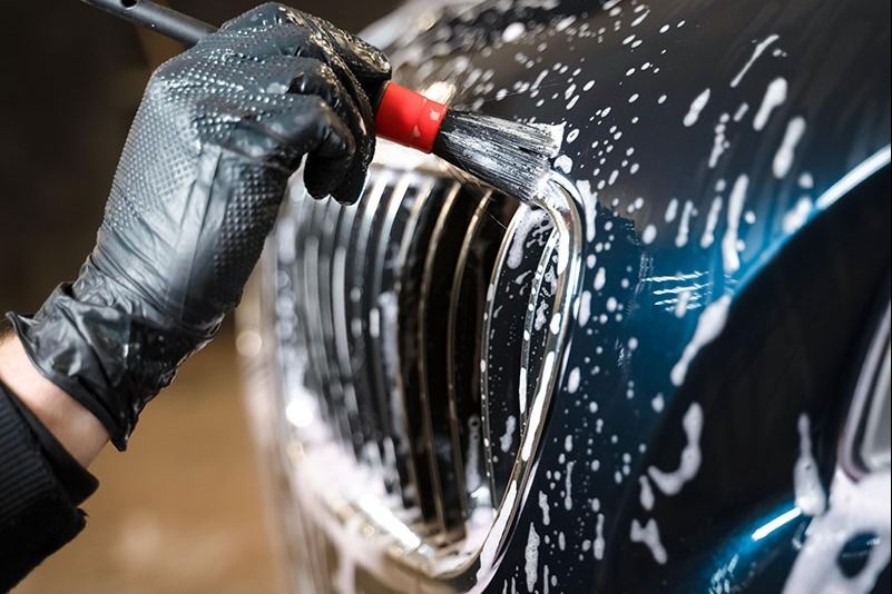 A black car is covered in foam at a car wash.