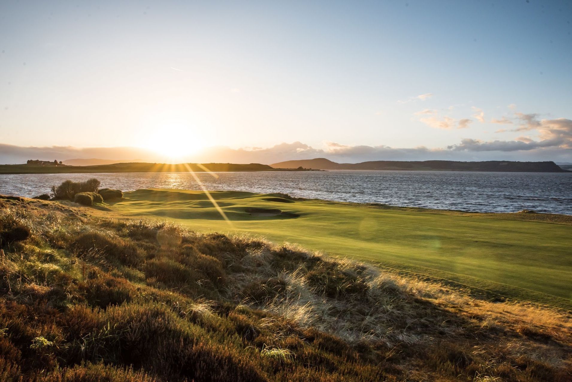 The sun is setting over a golf course with a lake in the background.
