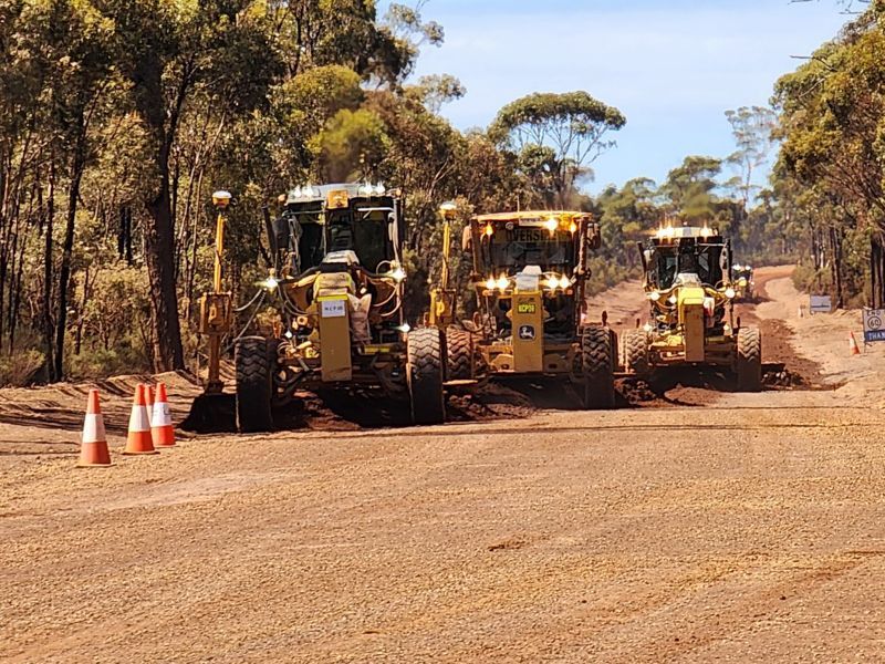 A group of construction vehicles are driving down a dirt road.