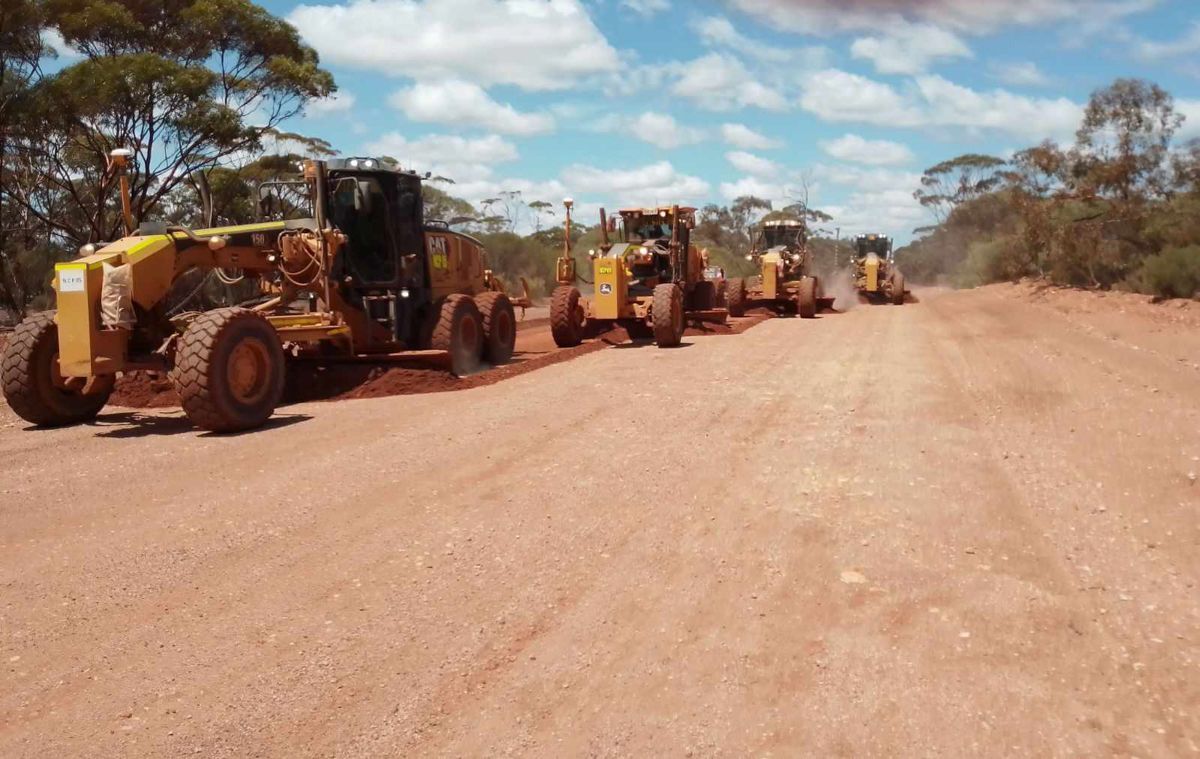 A group of construction vehicles are driving down a dirt road.
