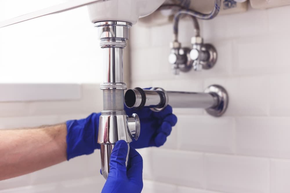 A Plumber is Fixing a Sink Pipe in a Bathroom — Mainline Plumbing & Civil Pty Ltd In Homebush, NSW