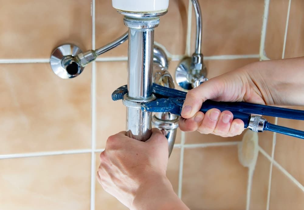 A Person is Fixing a Sink Pipe With a Wrench — Mainline Plumbing & Civil Pty Ltd In Homebush, NSW