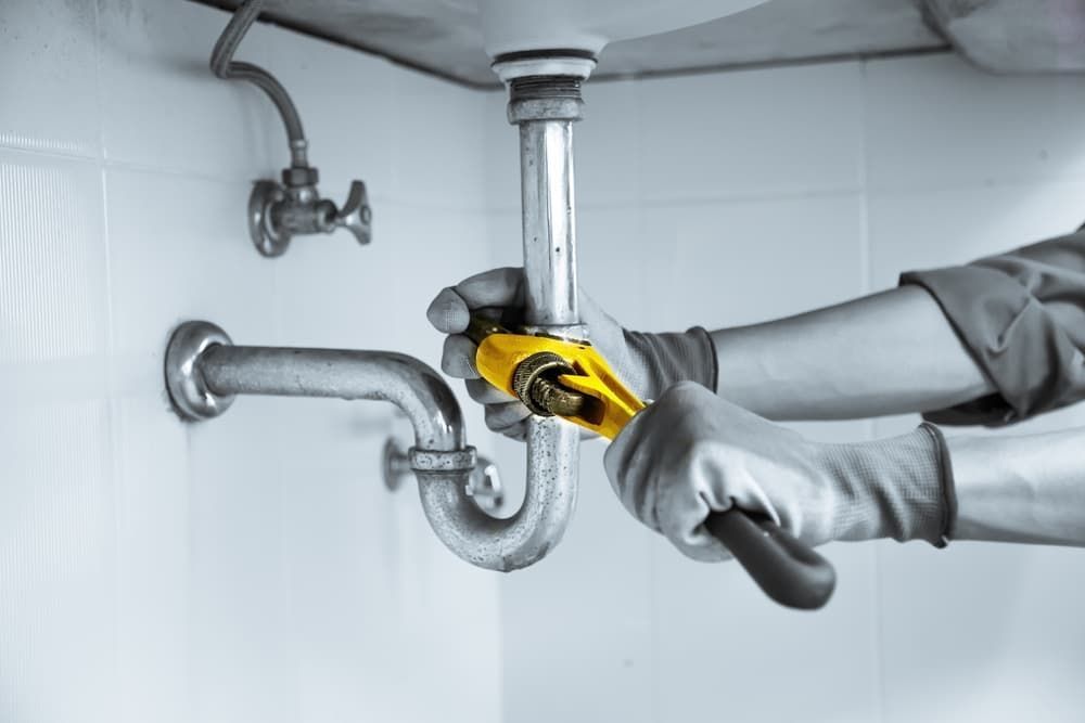 A Plumber is Fixing a Sink Pipe With a Wrench — Mainline Plumbing & Civil Pty Ltd In Wellington, NSW