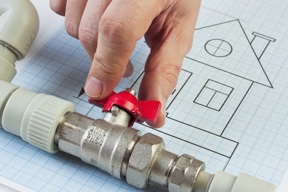A Person is Holding a Valve Over a Drawing of a House — Mainline Plumbing & Civil Pty Ltd In Wellington, NSW