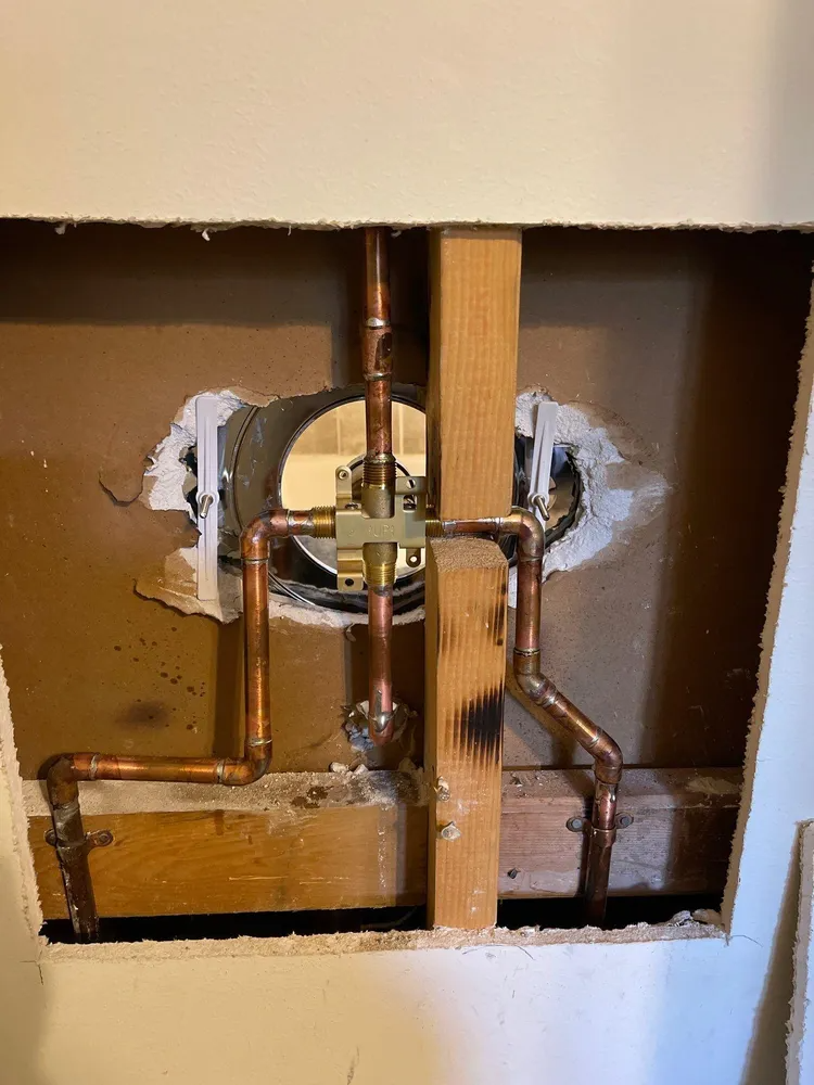 Open wall showing exposed plumbing pipes and a valve around a vertical wooden stud