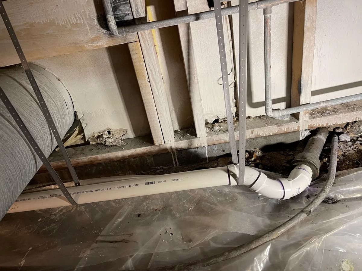 Damaged wall and exposed pipes above a plastic-covered floor in a construction area