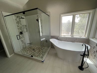 Modern bathroom with glass walk-in shower, freestanding tub, and large window with natural light