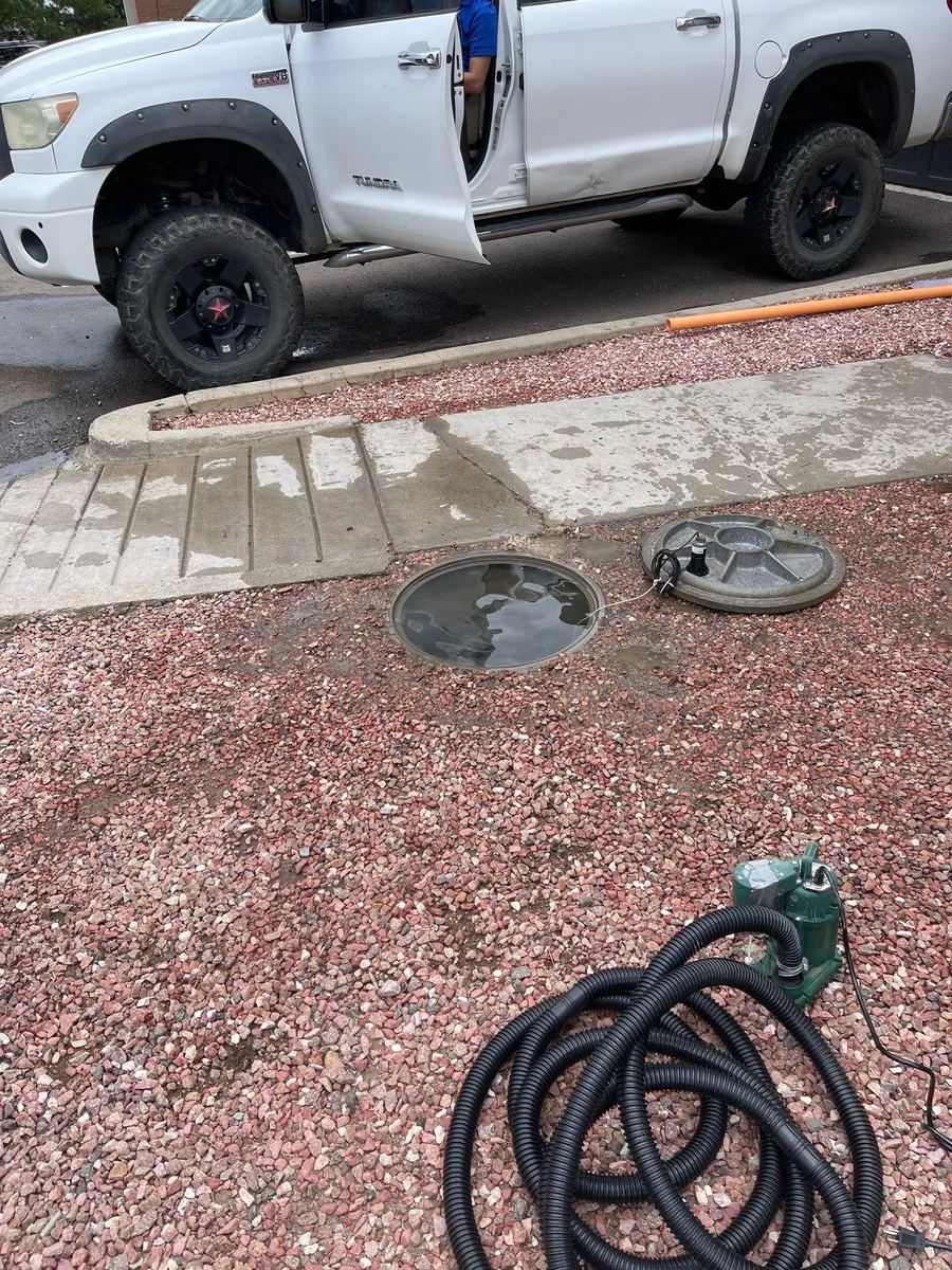 White pickup truck beside a gravel yard with a coiled hose and a green tool in the foreground