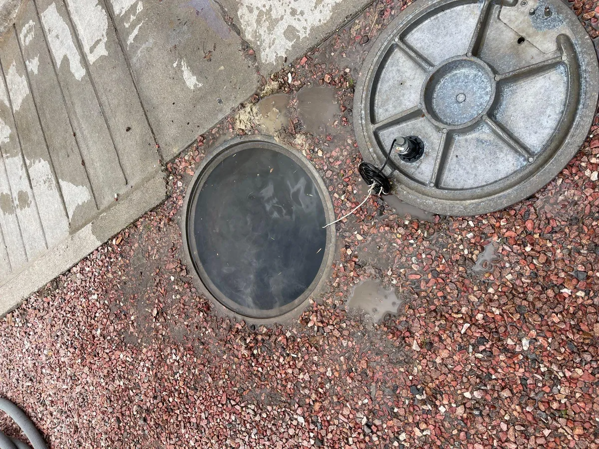 Outdoor utility access covers set in gravel beside a concrete sidewalk edge.