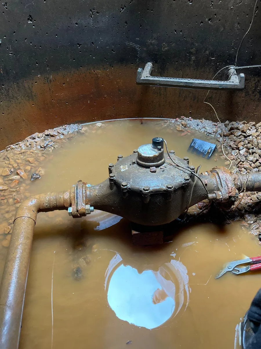 Rusty valve assembly in muddy water inside a dark pit