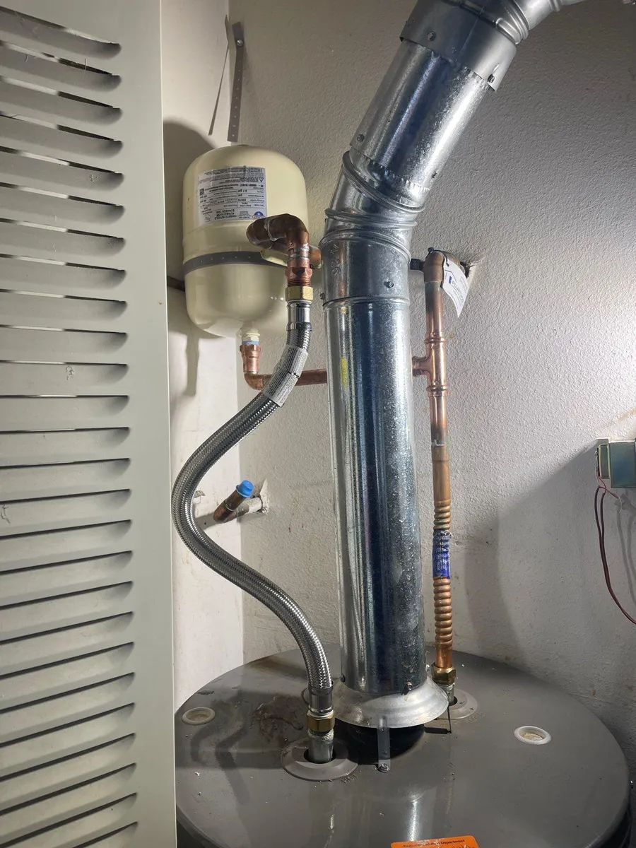 Water heater with metal venting and pipes in a utility closet.